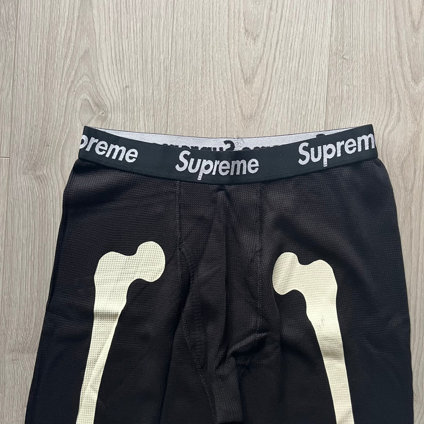  Supreme Hanes Bones Thermal Pant FW25 in black, crafted from 100% cotton. Features white skeletal bone prints running down both legs and a black elastic waistband with white Supreme branding throughout. Released October 23, 2025.
