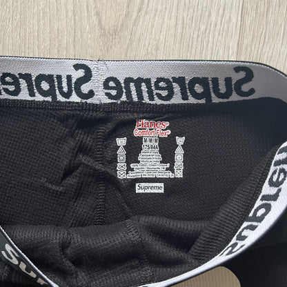  Supreme Hanes Bones Thermal Pant FW25 in black, crafted from 100% cotton. Features white skeletal bone prints running down both legs and a black elastic waistband with white Supreme branding throughout. Released October 23, 2025.