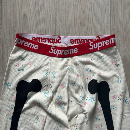 Supreme Hanes Bones Thermal Pant FW25 in natural/white with small floral all over print, crafted from 100% cotton. Features black skeletal bone prints running down both legs and a red elastic waistband with white Supreme branding throughout. Released October 23, 2025.