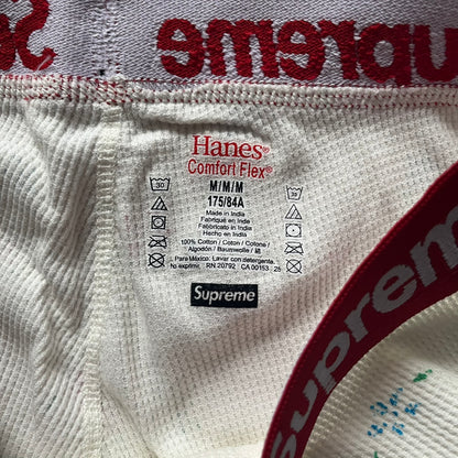 Supreme Hanes Bones Thermal Pant FW25 in natural/white with small floral all over print, crafted from 100% cotton. Features black skeletal bone prints running down both legs and a red elastic waistband with white Supreme branding throughout. Released October 23, 2025.