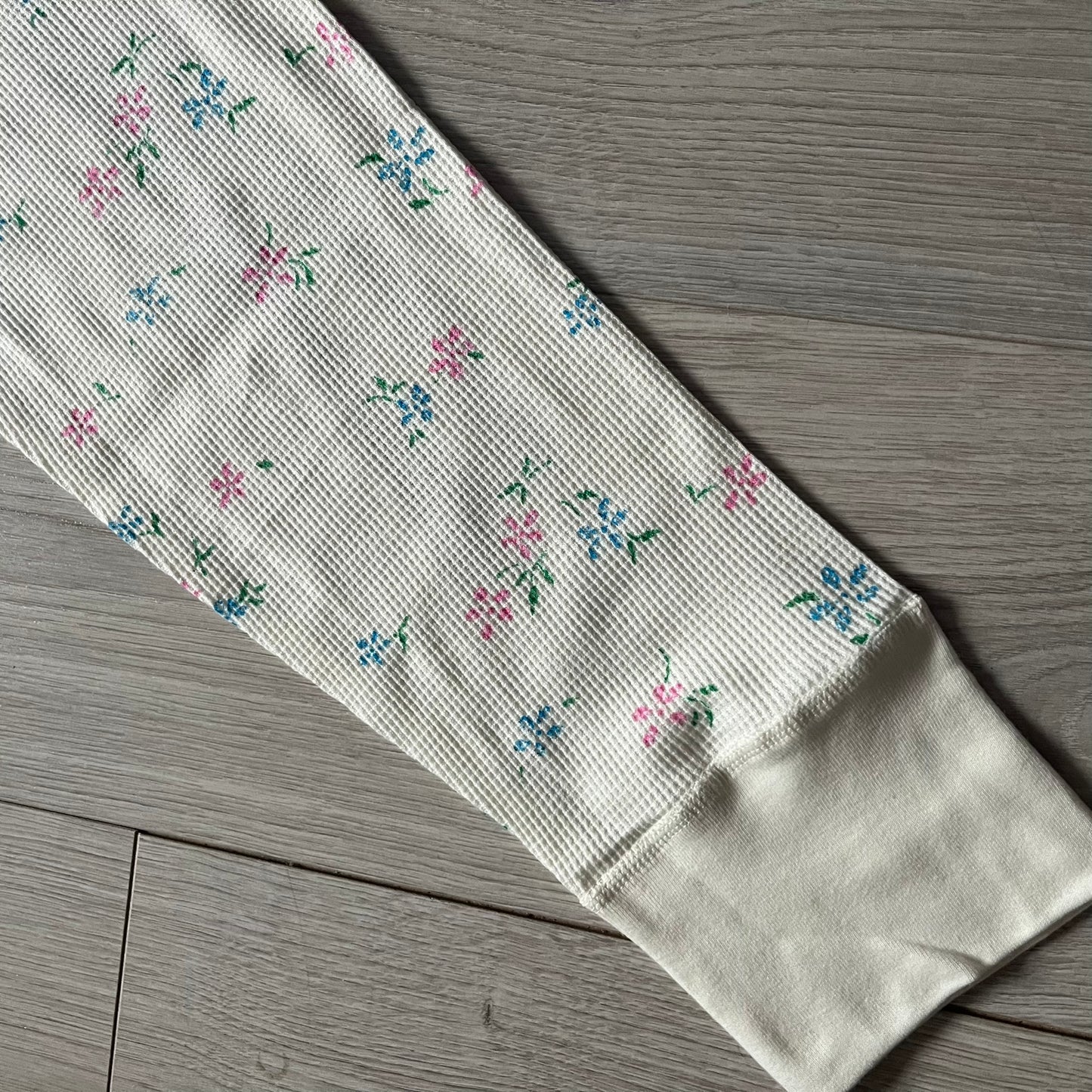 Supreme Hanes Bones Thermal Pant FW25 in natural/white with small floral all over print, crafted from 100% cotton. Features black skeletal bone prints running down both legs and a red elastic waistband with white Supreme branding throughout. Released October 23, 2025.