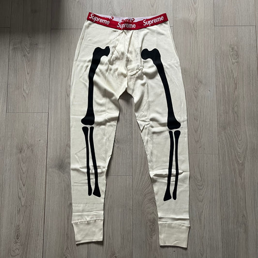Supreme Hanes Bones Thermal Pant FW25 in natural/white, crafted from 100% cotton. Features black skeletal bone prints running down both legs and a red elastic waistband with white Supreme branding throughout. Released October 23, 2025.