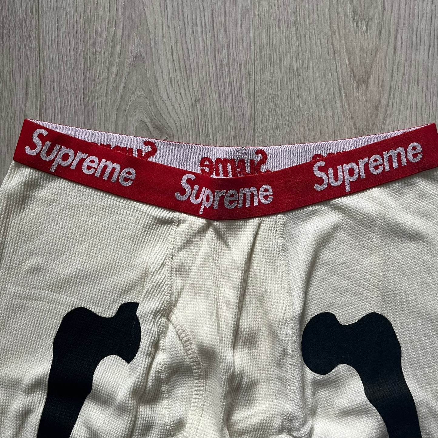 Supreme Hanes Bones Thermal Pant FW25 in natural/white, crafted from 100% cotton. Features black skeletal bone prints running down both legs and a red elastic waistband with white Supreme branding throughout. Released October 23, 2025.