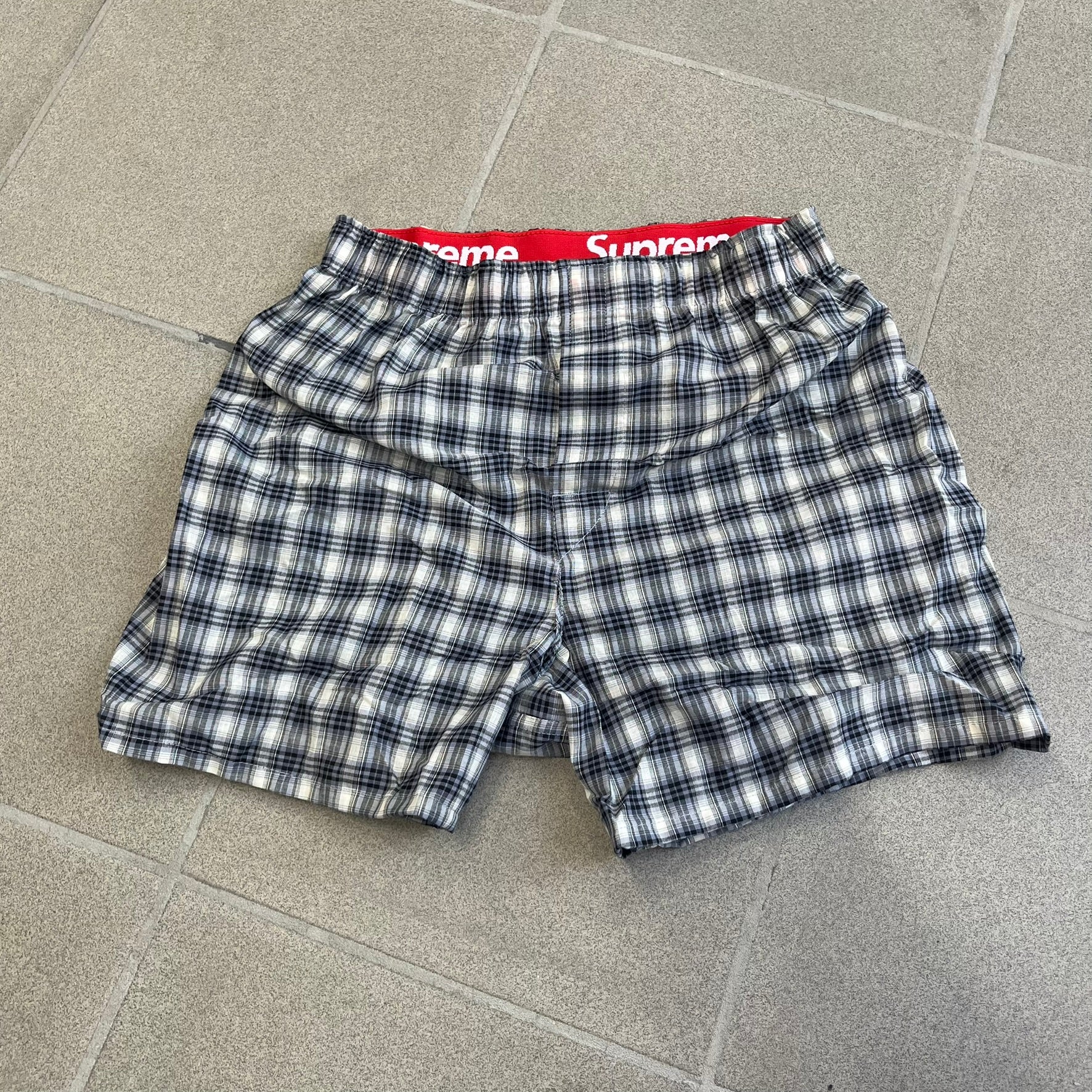 Supreme Hanes FW26 Plaid Boxers feature a plaid pattern and a red Supreme elastic waistband concealed inside. Made from 55% cotton and 45% polyester with Hanes Comfort Flex construction. Pink, grey, blue, and yellow colorways.