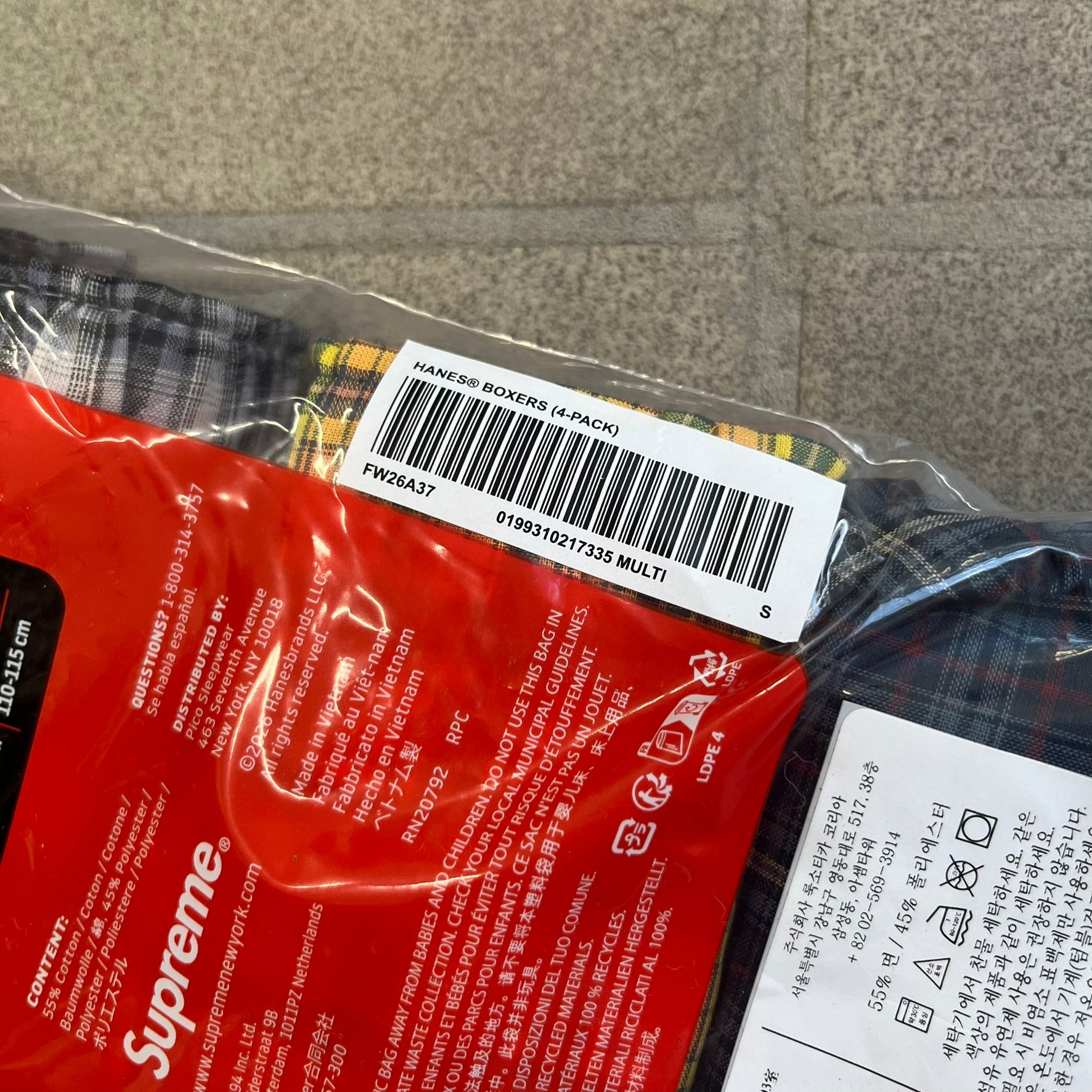 Supreme Hanes FW26 Plaid Boxers feature a plaid pattern and a red Supreme elastic waistband concealed inside. Made from 55% cotton and 45% polyester with Hanes Comfort Flex construction. Pink, grey, blue, and yellow colorways.