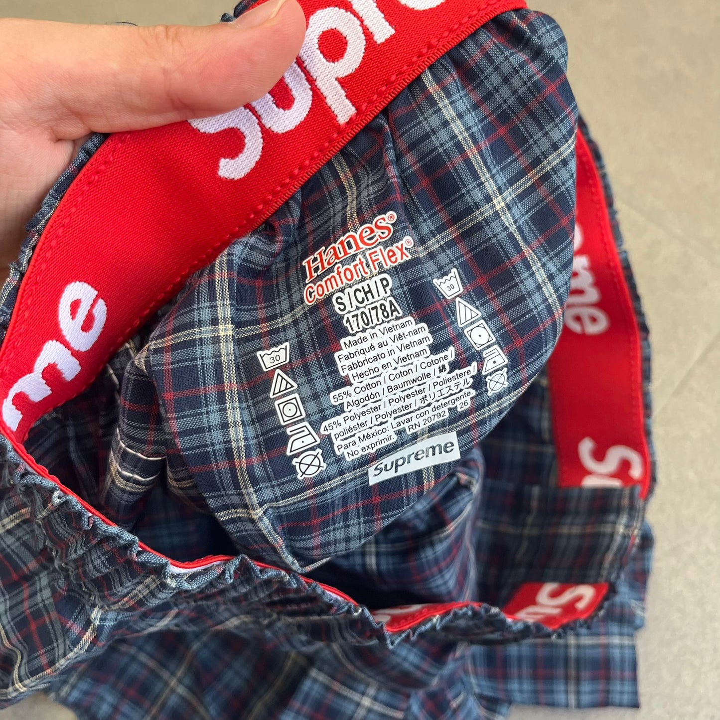 Supreme Hanes FW26 Plaid Boxers feature a plaid pattern and a red Supreme elastic waistband concealed inside. Made from 55% cotton and 45% polyester with Hanes Comfort Flex construction. Pink, grey, blue, and yellow colorways.
