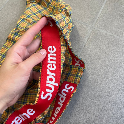 Supreme Hanes FW26 Plaid Boxers feature a plaid pattern and a red Supreme elastic waistband concealed inside. Made from 55% cotton and 45% polyester with Hanes Comfort Flex construction. Pink, grey, blue, and yellow colorways.