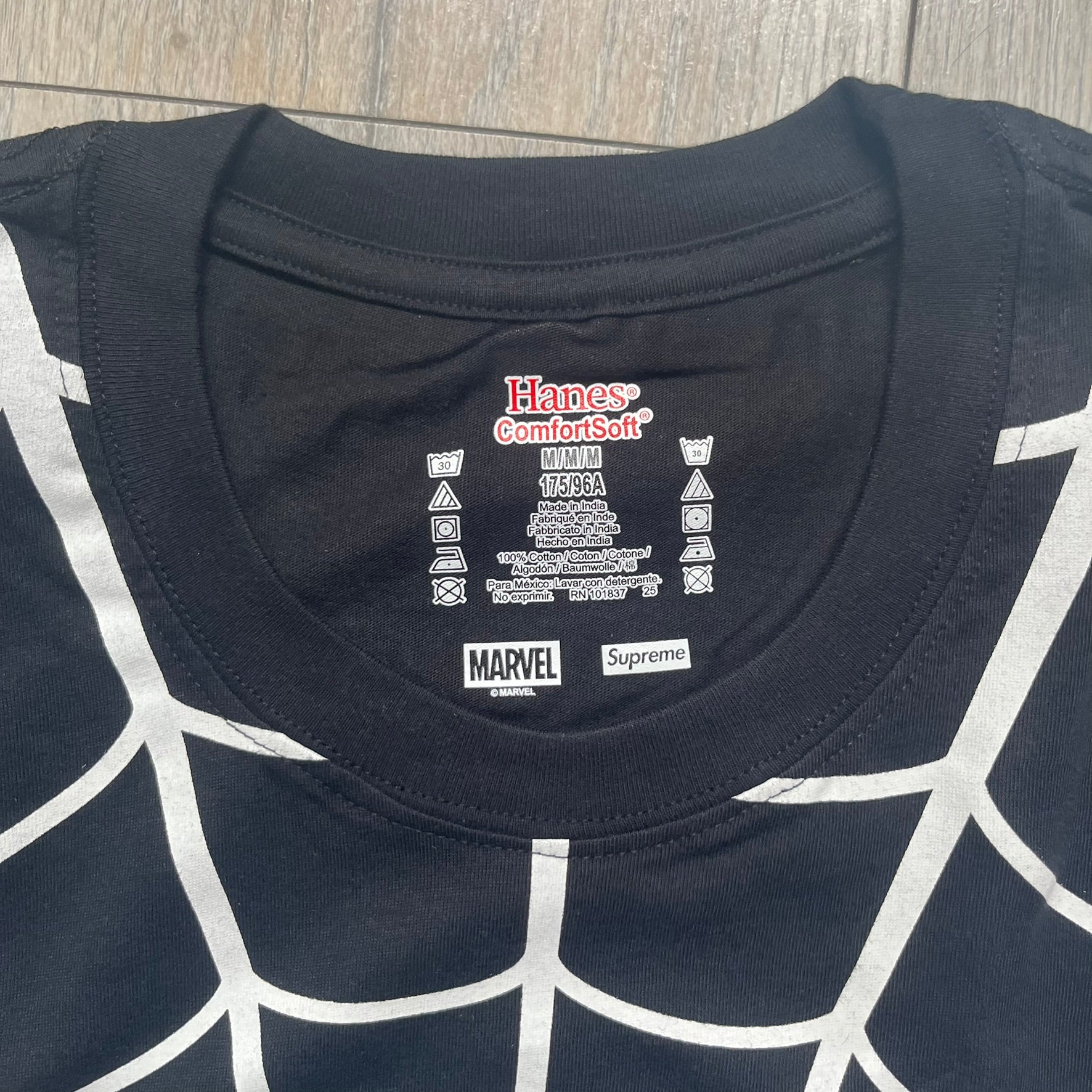 Supreme Hanes SS26 Spider-Man Black Tagless Tee is a black all-cotton crewneck T-shirt from the Spring/Summer 2026 collection, produced on a Hanes tagless blank. The shirt features an all-over white web print covering the front, back, and sleeves, with a small red Supreme stamp logo printed near the bottom corner.