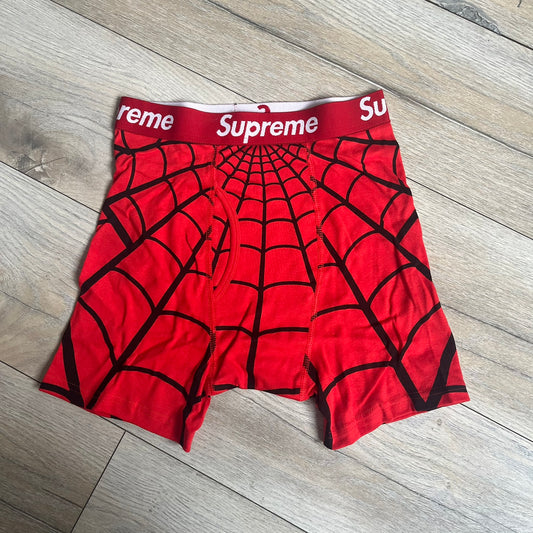 Supreme Hanes SS26 Spider-Man Red Boxer Briefs are made of cotton with a stretch fit. Features a red elastic waistband with white Supreme logo text and an all-over black web print. Classic Hanes base model a Spider-Man twist.