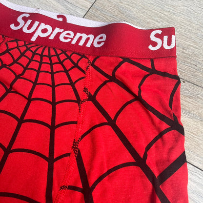 Supreme Hanes SS26 Spider-Man Red Boxer Briefs are made of cotton with a stretch fit. Features a red elastic waistband with white Supreme logo text and an all-over black web print. Classic Hanes base model a Spider-Man twist.