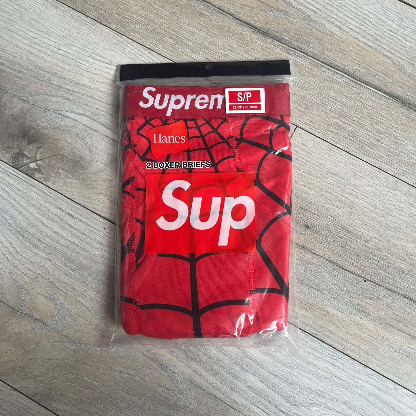 Supreme Hanes SS26 Spider-Man Red Boxer Briefs are made of cotton with a stretch fit. Features a red elastic waistband with white Supreme logo text and an all-over black web print. Classic Hanes base model a Spider-Man twist.