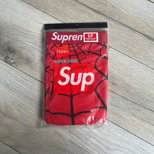 Supreme Hanes SS26 Spider-Man Red Boxer Briefs are made of cotton with a stretch fit. Features a red elastic waistband with white Supreme logo text and an all-over black web print. Classic Hanes base model a Spider-Man twist.