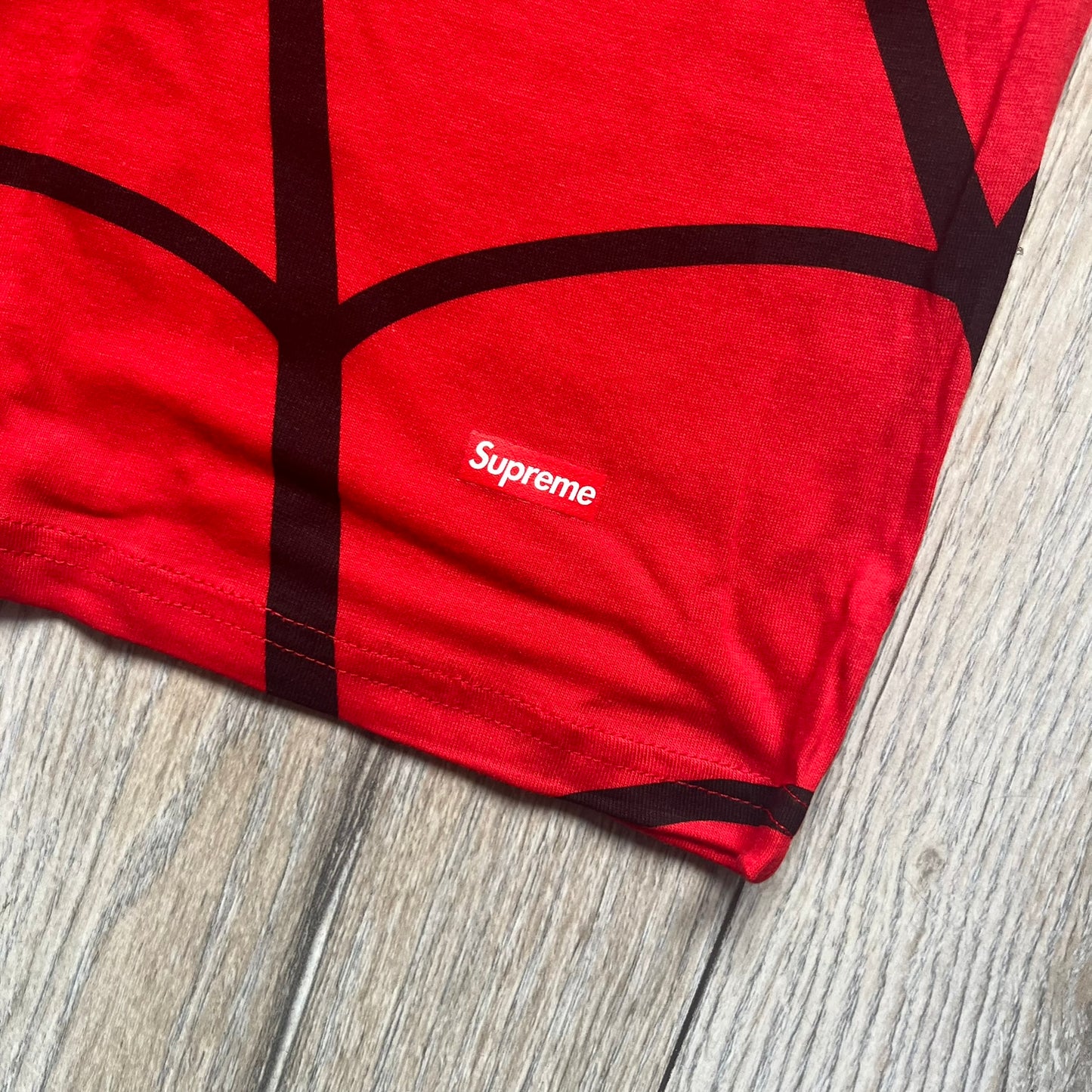 Supreme Hanes SS26 Spider-Man Red Tagless Tee is a red all-cotton crewneck T-shirt from the Spring/Summer 2026 collection, produced on a Hanes tagless blank. The shirt features an all-over black web print covering the front, back, and sleeves, with a small red Supreme stamp logo printed near the bottom corner.