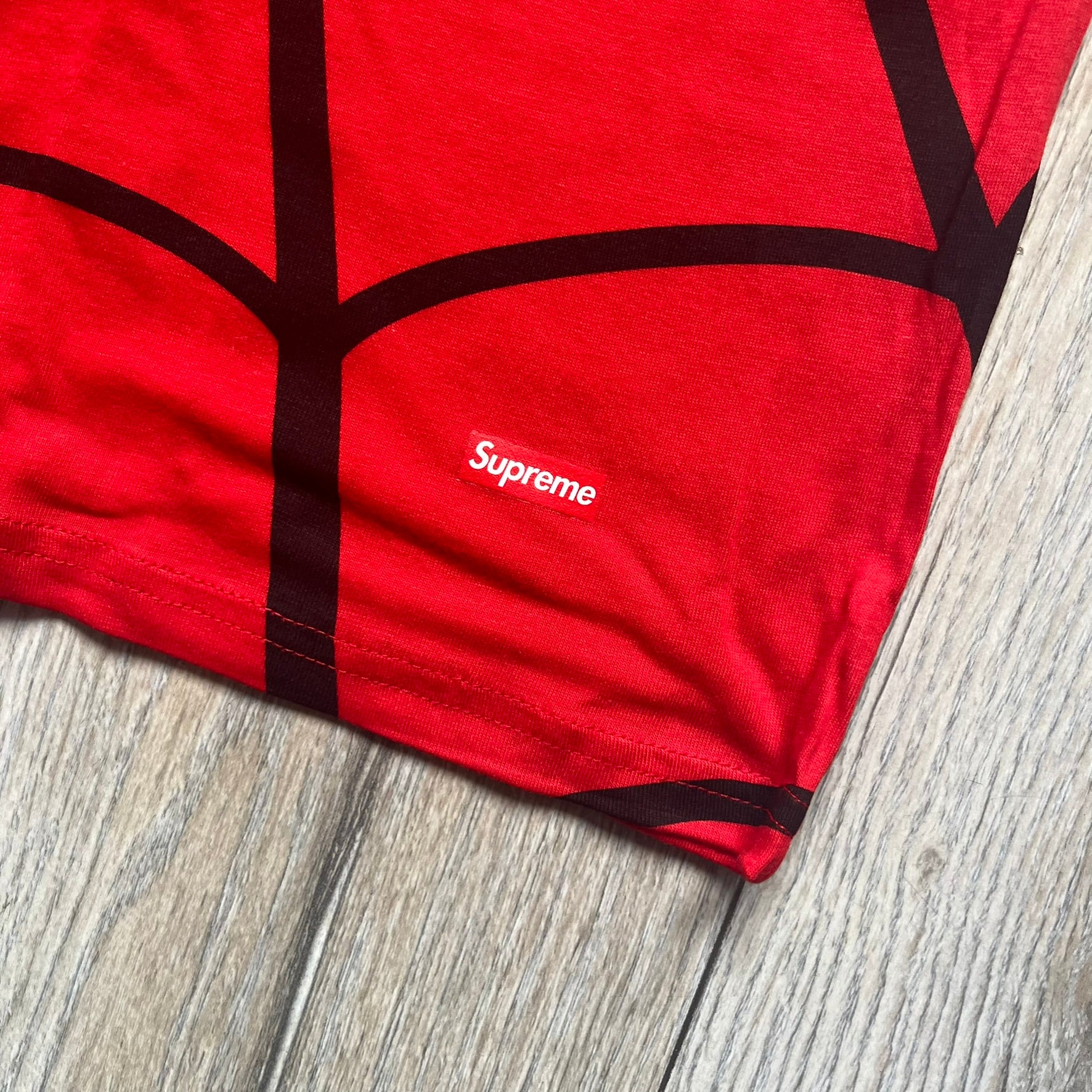 Supreme Hanes SS26 Spider-Man Red Tagless Tee is a red all-cotton crewneck T-shirt from the Spring/Summer 2026 collection, produced on a Hanes tagless blank. The shirt features an all-over black web print covering the front, back, and sleeves, with a small red Supreme stamp logo printed near the bottom corner.