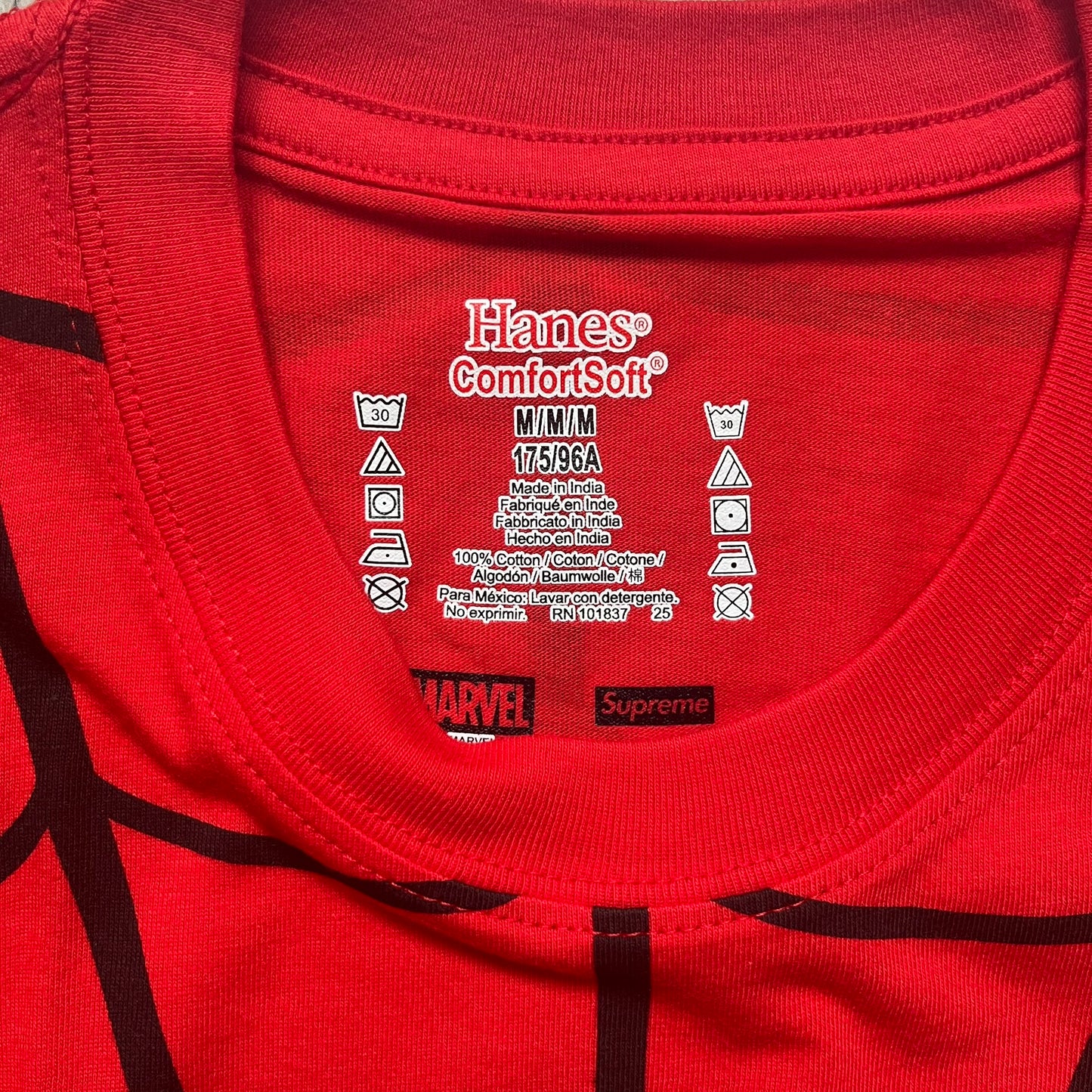 Supreme Hanes SS26 Spider-Man Red Tagless Tee is a red all-cotton crewneck T-shirt from the Spring/Summer 2026 collection, produced on a Hanes tagless blank. The shirt features an all-over black web print covering the front, back, and sleeves, with a small red Supreme stamp logo printed near the bottom corner.