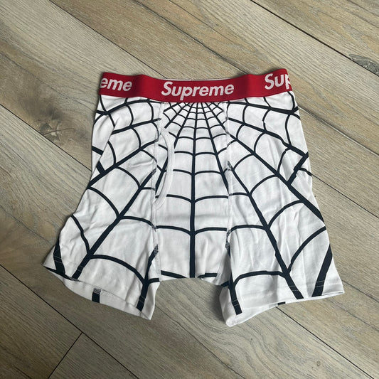 Supreme Hanes SS26 Spider-Man White Boxer Briefs are made of cotton with a stretch fit. Features a red elastic waistband with white Supreme logo text and an all-over black web print. Classic Hanes base model a Spider-Man twist.