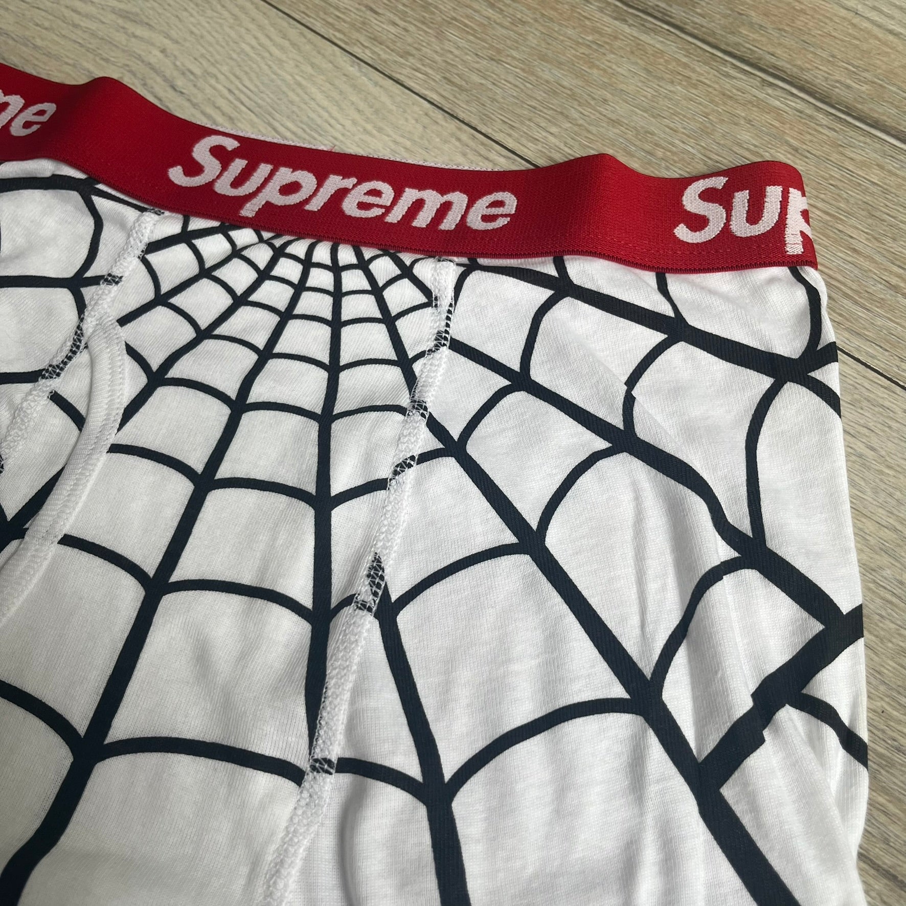 Supreme Hanes SS26 Spider-Man White Boxer Briefs are made of cotton with a stretch fit. Features a red elastic waistband with white Supreme logo text and an all-over black web print. Classic Hanes base model a Spider-Man twist.