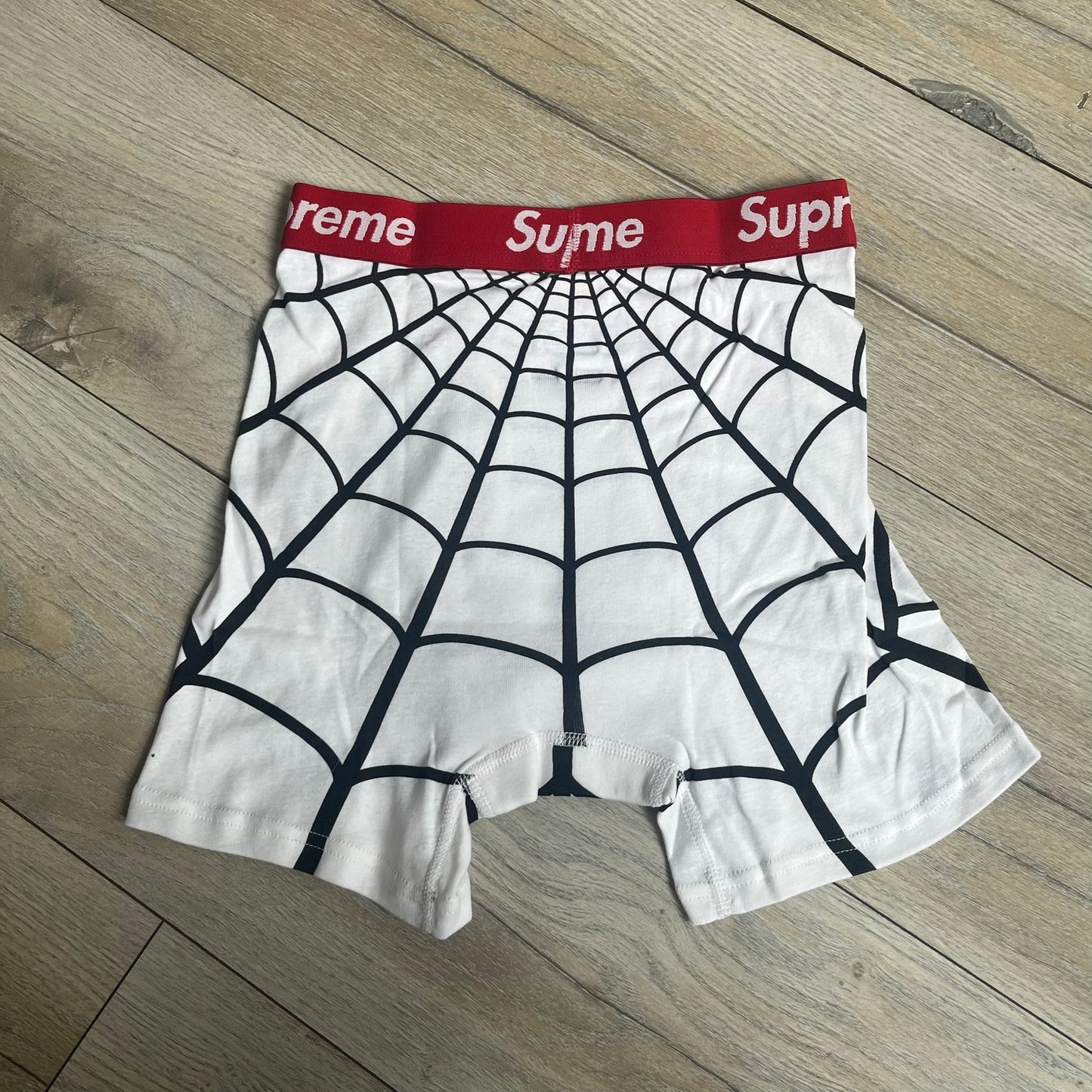 Supreme Hanes SS26 Spider-Man White Boxer Briefs are made of cotton with a stretch fit. Features a red elastic waistband with white Supreme logo text and an all-over black web print. Classic Hanes base model a Spider-Man twist.