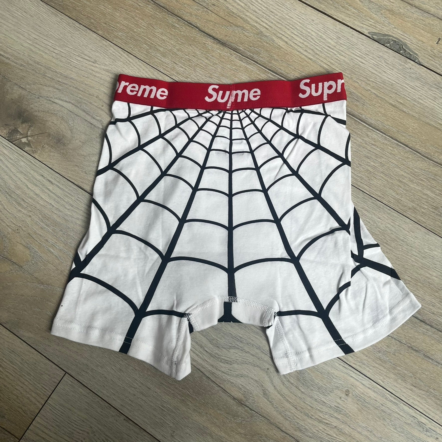 Supreme Hanes SS26 Spider-Man White Boxer Briefs are made of cotton with a stretch fit. Features a red elastic waistband with white Supreme logo text and an all-over black web print. Classic Hanes base model a Spider-Man twist.