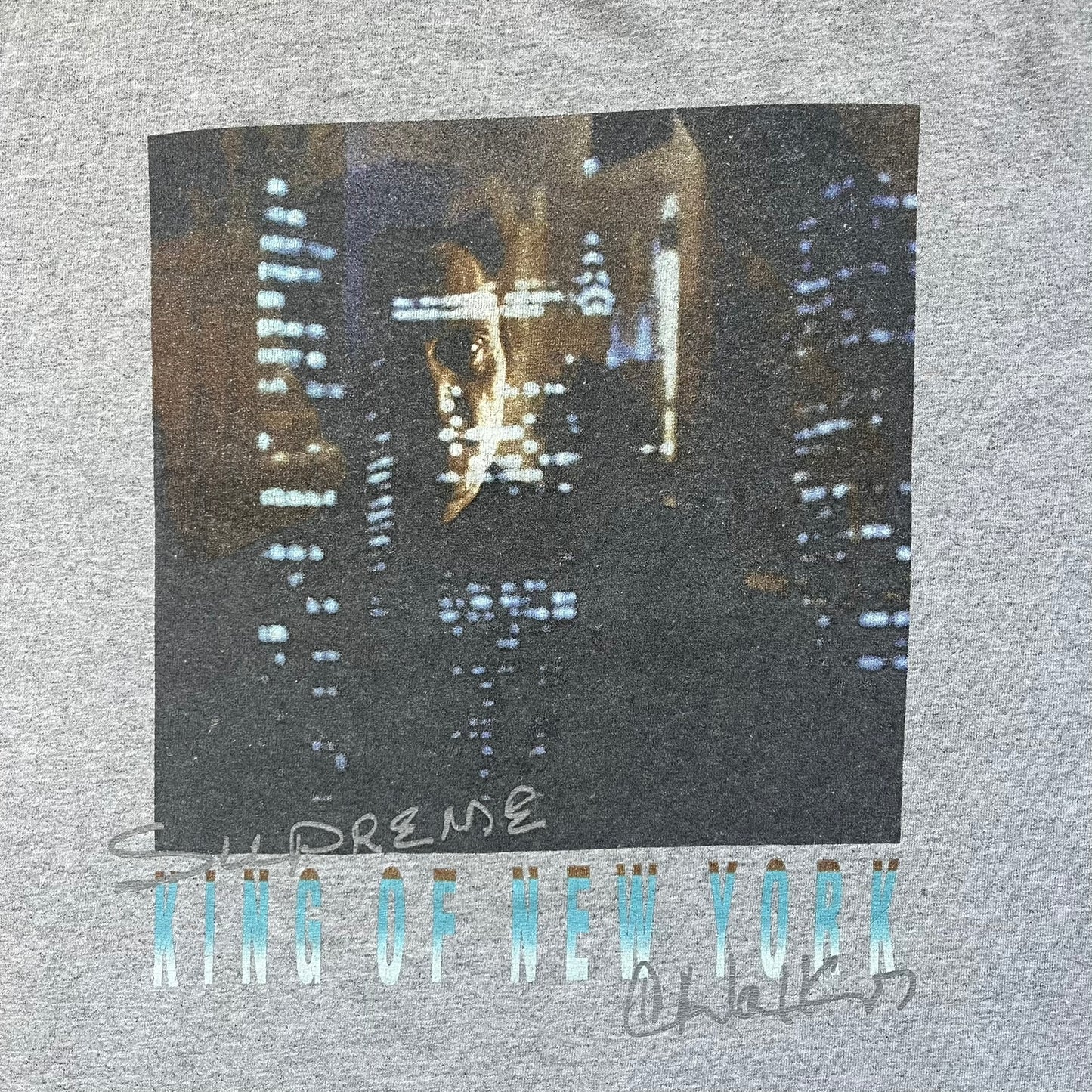 Supreme King of New York SS19 Gray Tee is a heather gray T-shirt released on February 21, 2019, as part of the SS19 collection. The front features an edited King of New York movie cover graphic with Christopher Walken’s name removed and replaced by handwritten-style “Supreme” and “C. Walken” text. The print is based on the original film cover artwork.