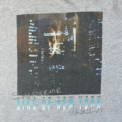 Supreme King of New York SS19 Gray Tee is a heather gray T-shirt released on February 21, 2019, as part of the SS19 collection. The front features an edited King of New York movie cover graphic with Christopher Walken’s name removed and replaced by handwritten-style “Supreme” and “C. Walken” text. The print is based on the original film cover artwork.