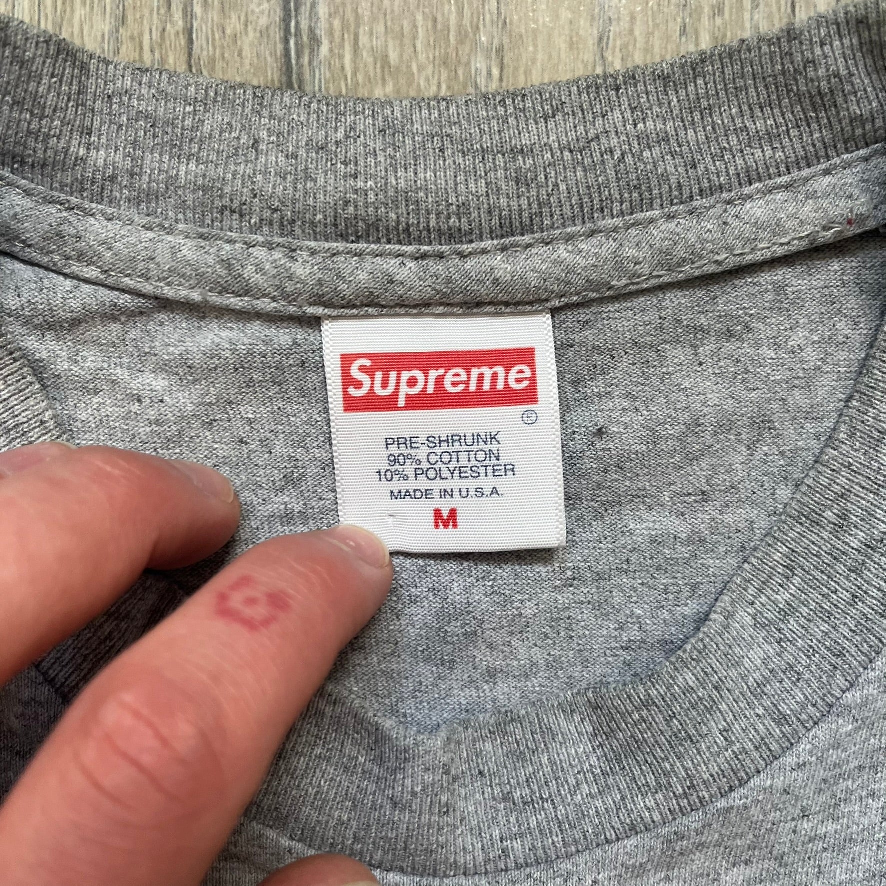 Supreme King of New York SS19 Gray Tee is a heather gray T-shirt released on February 21, 2019, as part of the SS19 collection. The front features an edited King of New York movie cover graphic with Christopher Walken’s name removed and replaced by handwritten-style “Supreme” and “C. Walken” text. The print is based on the original film cover artwork.