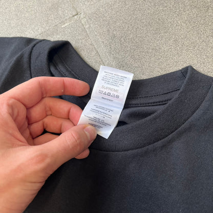 Supreme Larry Clark FW26 Black Neighbor Tee is a black, 100% cotton T-shirt featuring a front photograph by Larry Clark of Gabbriette (Gabriella Leigh Bechtel) seated in underwear on a bed beside a red Supreme skateboard. The back displays hand-drawn-style white text reading "Love Thy Neighbor, Larry Clark 2026, Supreme."
