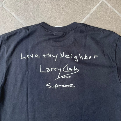 Product description:
Supreme Larry Clark FW26 Black Neighbor Tee is a black, 100% cotton T-shirt featuring a front photograph by Larry Clark of Gabbriette (Gabriella Leigh Bechtel) seated in underwear on a bed beside a red Supreme skateboard. The back displays hand-drawn-style white text reading "Love Thy Neighbor, Larry Clark 2026, Supreme."