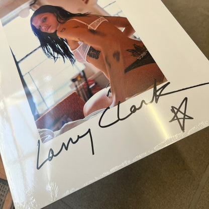 Supreme Larry Clark FW26 Multicolor Zine is a 48-page white zine with original photography by Larry Clark, including a poster insert. The cover features Gabbriette (Gabriella Leigh Bechtel) styled in Supreme underwear against a USA flag backdrop, with hand-drawn "Supreme" text scribbled at the top and "Larry Clark" with a star at the bottom, while the back displays a small Supreme logo.