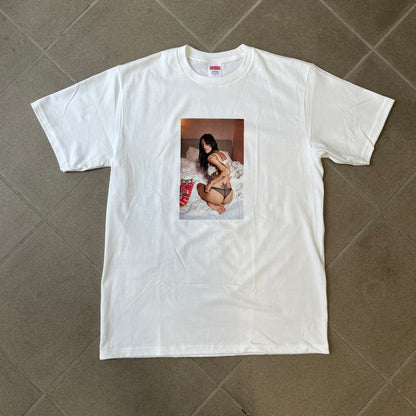Supreme Larry Clark FW26 White Neighbor Tee is a white, 100% cotton T-shirt featuring a front photograph by Larry Clark of Gabbriette (Gabriella Leigh Bechtel) seated in underwear on a bed beside a red Supreme skateboard. The back displays hand-drawn-style black text reading "Love Thy Neighbor, Larry Clark 2026, Supreme."
