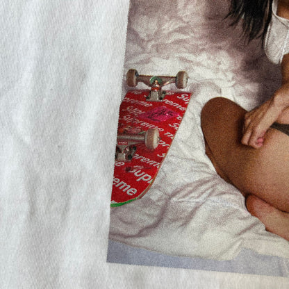Supreme Larry Clark FW26 White Neighbor Tee is a white, 100% cotton T-shirt featuring a front photograph by Larry Clark of Gabbriette (Gabriella Leigh Bechtel) seated in underwear on a bed beside a red Supreme skateboard. The back displays hand-drawn-style black text reading "Love Thy Neighbor, Larry Clark 2026, Supreme."