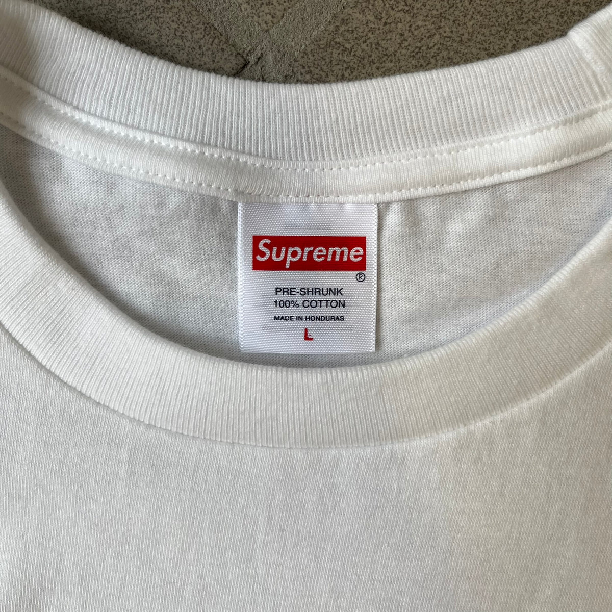 Supreme Larry Clark FW26 White Neighbor Tee is a white, 100% cotton T-shirt featuring a front photograph by Larry Clark of Gabbriette (Gabriella Leigh Bechtel) seated in underwear on a bed beside a red Supreme skateboard. The back displays hand-drawn-style black text reading "Love Thy Neighbor, Larry Clark 2026, Supreme."