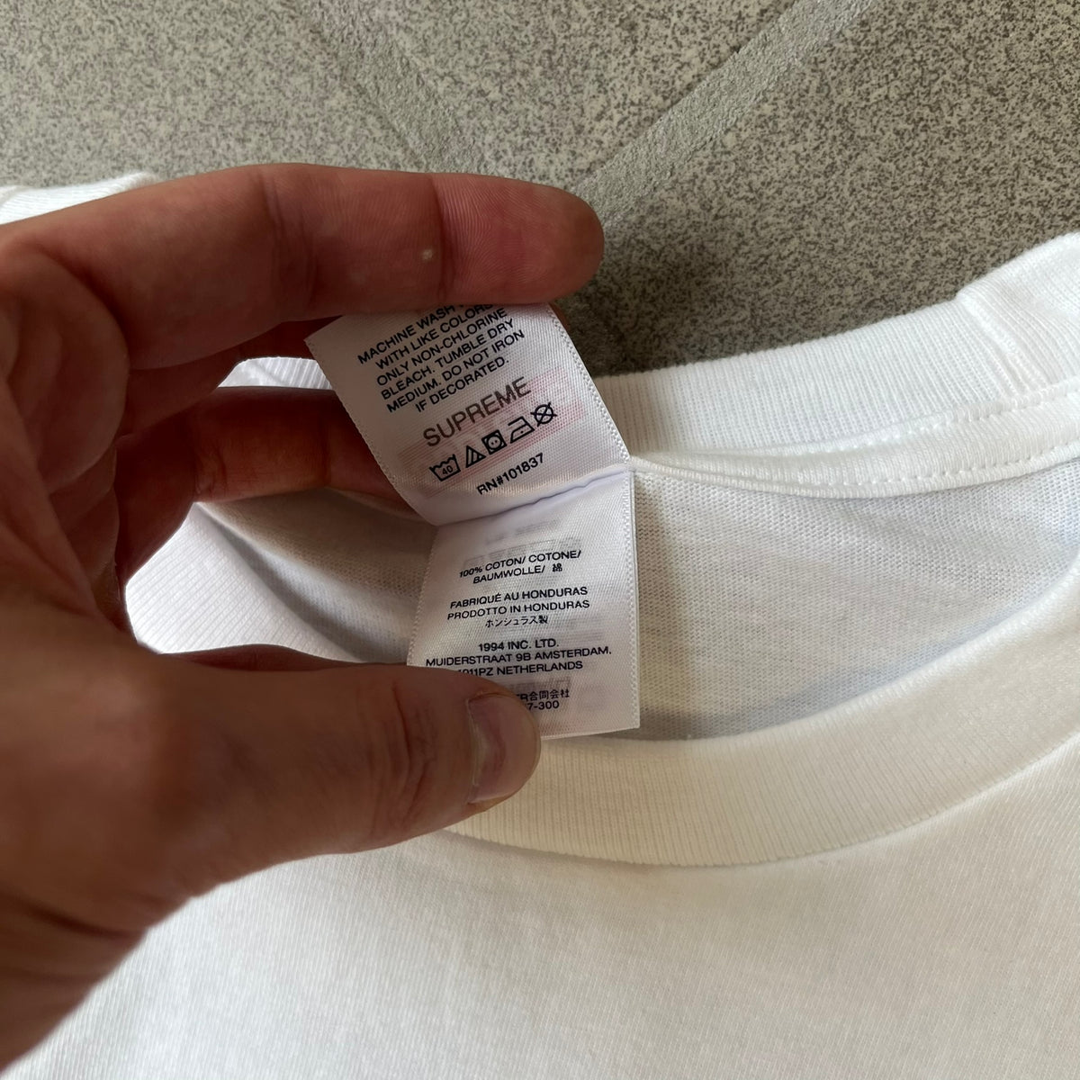 Supreme Larry Clark FW26 White Neighbor Tee is a white, 100% cotton T-shirt featuring a front photograph by Larry Clark of Gabbriette (Gabriella Leigh Bechtel) seated in underwear on a bed beside a red Supreme skateboard. The back displays hand-drawn-style black text reading "Love Thy Neighbor, Larry Clark 2026, Supreme."