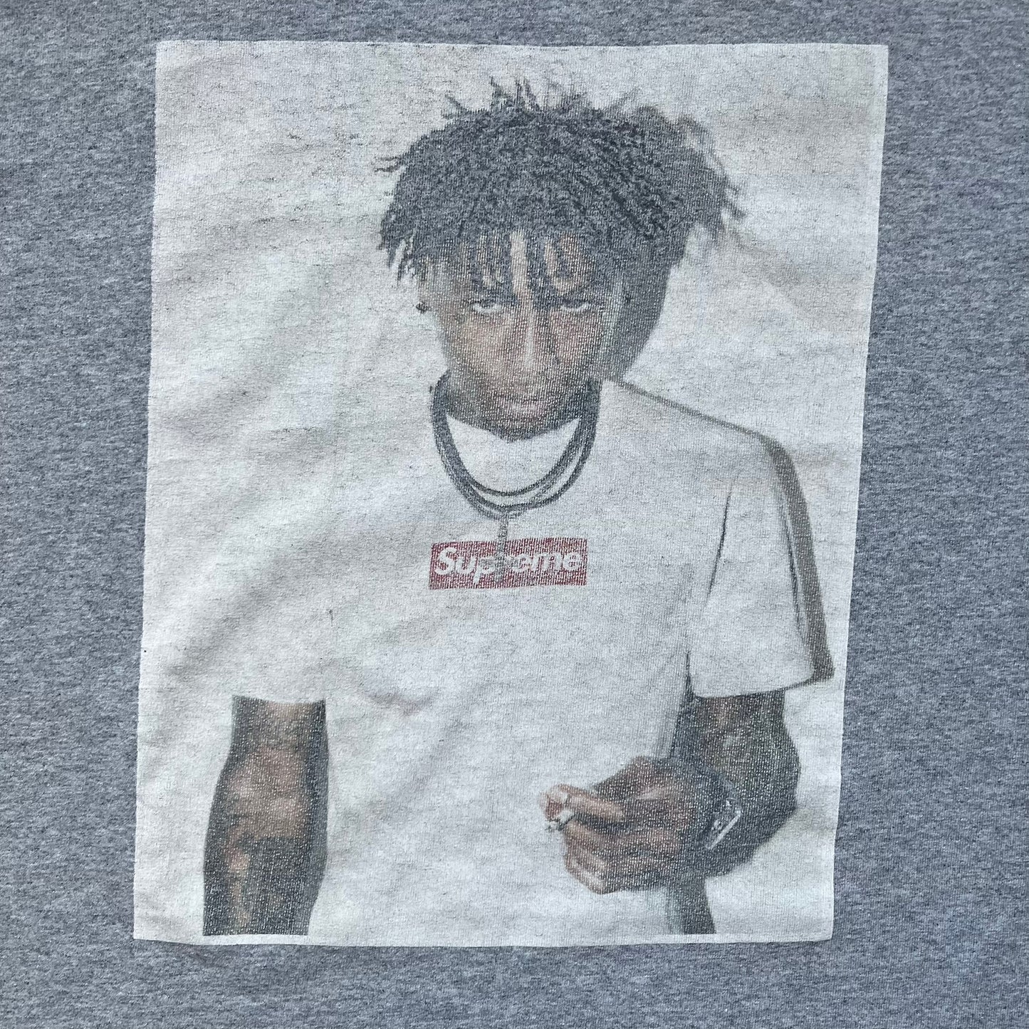 Supreme NBA Youngboy FW23 Gray Tee is a gray crew-neck T-shirt made in the USA from 100% cotton. The front features a multicolor graphic print of NBA Youngboy wearing the Supreme Box Logo tee. The shirt has short sleeves and a regular fit.