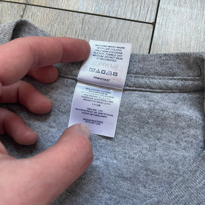 Supreme NBA Youngboy FW23 Gray Tee is a gray crew-neck T-shirt made in the USA from 100% cotton. The front features a multicolor graphic print of NBA Youngboy wearing the Supreme Box Logo tee. The shirt has short sleeves and a regular fit.