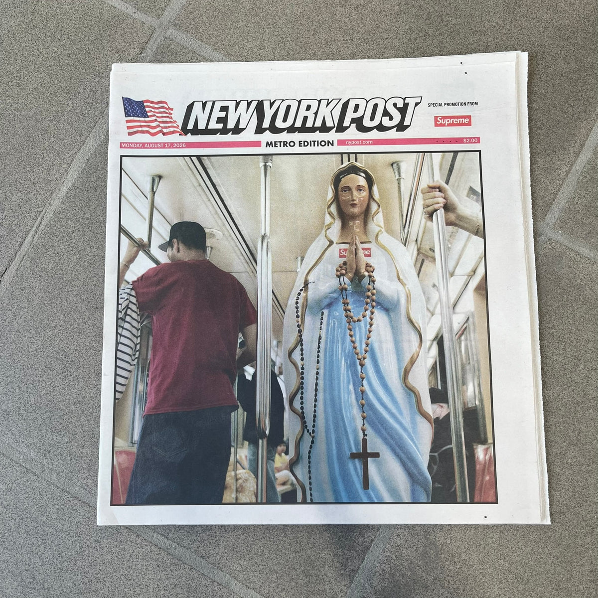 Supreme New York Post Newspaper “Late City Final Edition” from Fall/Winter 2026, released on August 17th, 2026. Features the features a religious statue with iconic Supreme box logo printed on it. On the back there's a "Deliver US From Evil". Includes the full original newspaper, with only the cover designed by Supreme.