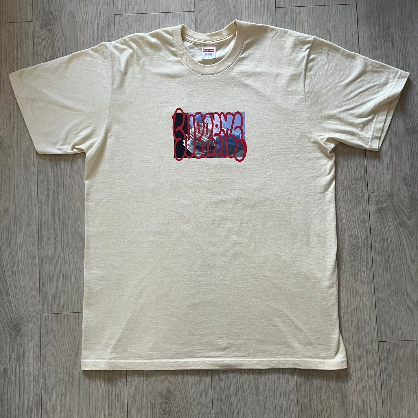 Natural Supreme tee from the FW23 season showcasing the “Payment” design. The front graphic depicts a pile of GBP banknotes with a large red graffiti-style Supreme tag layered across. A clean and minimalistic yet striking piece from the collection.