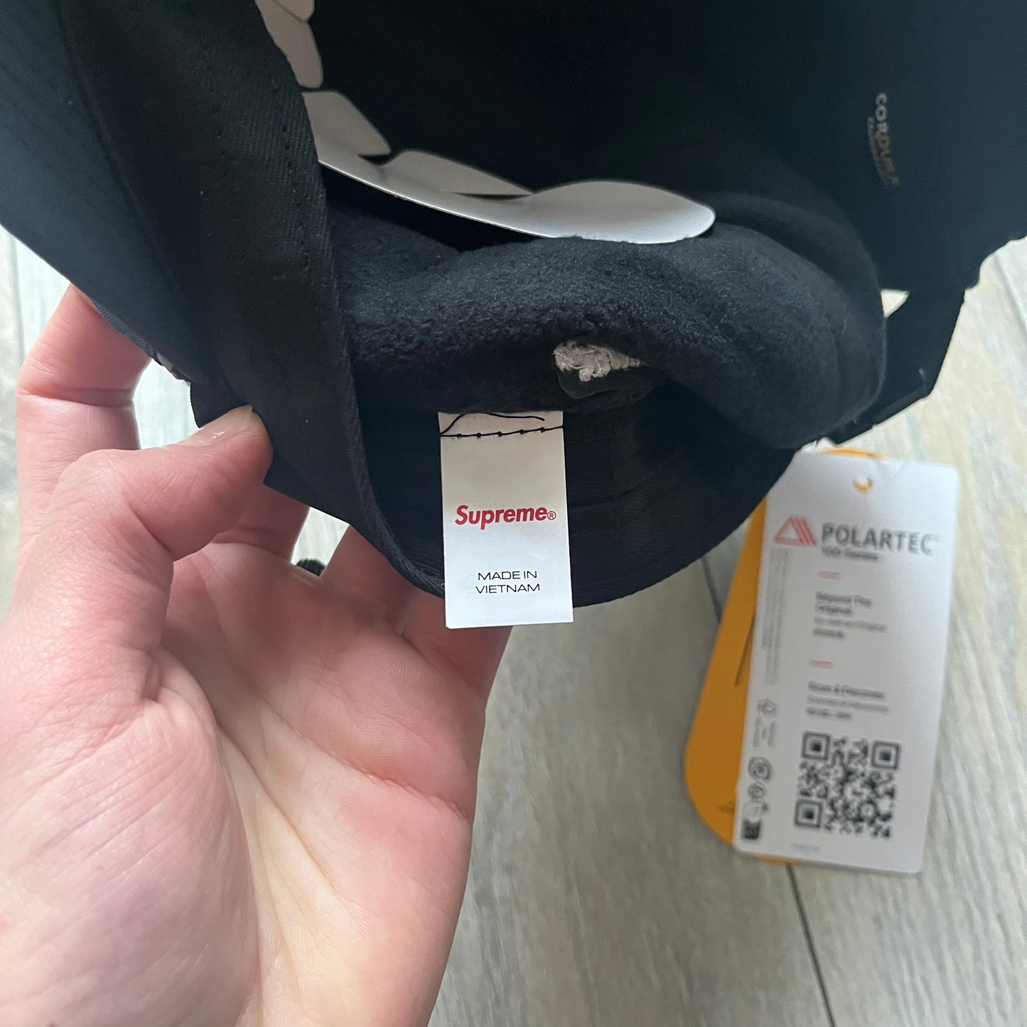 Supreme FW25 camp cap constructed from water-resistant Cordura® Advanced Fabrics nylon with a nylon and polyester shell. Lined with Polartec® 200 fleece for insulation, featuring packable earflaps secured with an interior elastic shockcord. Details include a webbing strap closure, 3M reflective piping, embroidered logos on the sides, and a classic Supreme box logo at the front. Finished in black.