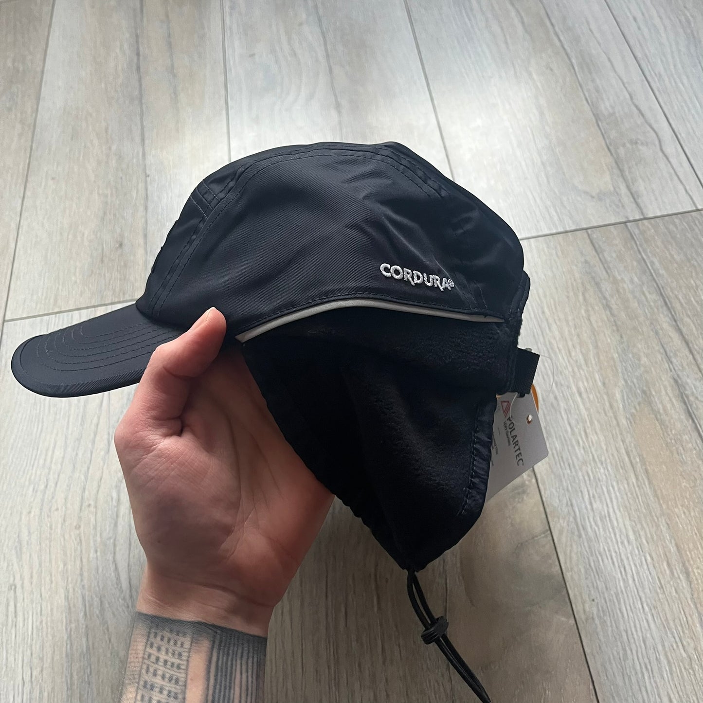 Supreme FW25 camp cap constructed from water-resistant Cordura® Advanced Fabrics nylon with a nylon and polyester shell. Lined with Polartec® 200 fleece for insulation, featuring packable earflaps secured with an interior elastic shockcord. Details include a webbing strap closure, 3M reflective piping, embroidered logos on the sides, and a classic Supreme box logo at the front. Finished in black.