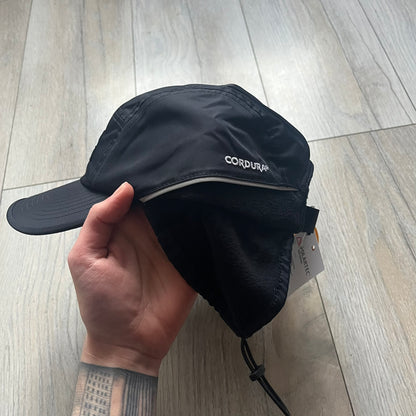 Supreme FW25 camp cap constructed from water-resistant Cordura® Advanced Fabrics nylon with a nylon and polyester shell. Lined with Polartec® 200 fleece for insulation, featuring packable earflaps secured with an interior elastic shockcord. Details include a webbing strap closure, 3M reflective piping, embroidered logos on the sides, and a classic Supreme box logo at the front. Finished in black.