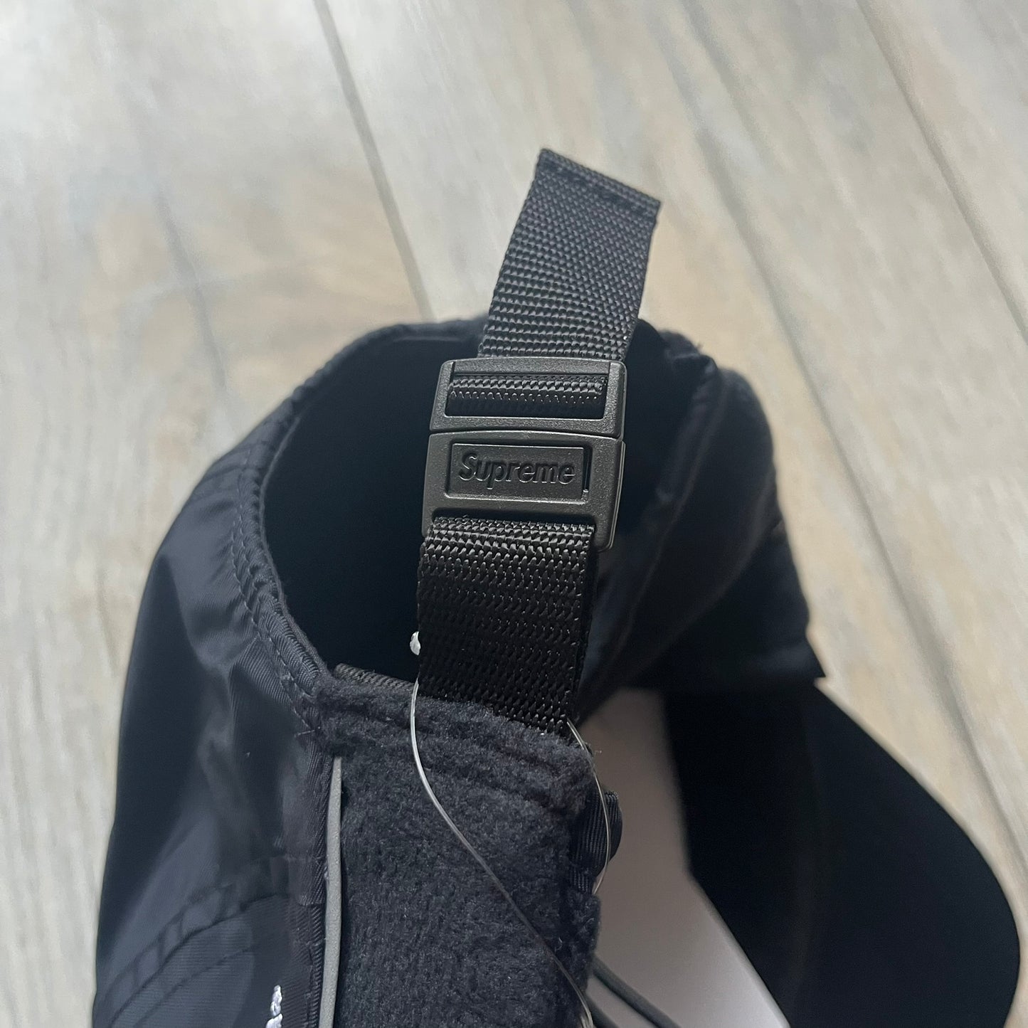 Supreme FW25 camp cap constructed from water-resistant Cordura® Advanced Fabrics nylon with a nylon and polyester shell. Lined with Polartec® 200 fleece for insulation, featuring packable earflaps secured with an interior elastic shockcord. Details include a webbing strap closure, 3M reflective piping, embroidered logos on the sides, and a classic Supreme box logo at the front. Finished in black.