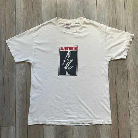Supreme SS05 STAX Records White Gun Tee is a white short-sleeve T-shirt from the Spring/Summer 2005 collection. The front features a modified Stax Records-inspired logo with “Supreme” in red and a hand holding a gun graphic. This piece is super rare.