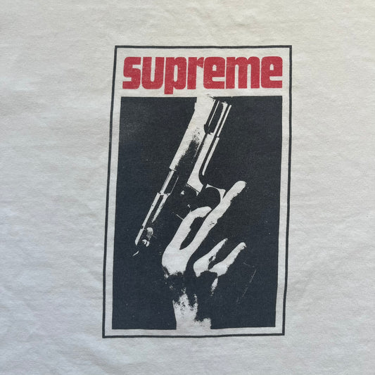 Supreme SS05 STAX Records White Gun Tee is a white short-sleeve T-shirt from the Spring/Summer 2005 collection. The front features a modified Stax Records-inspired logo with “Supreme” in red and a hand holding a gun graphic. This piece is super rare.