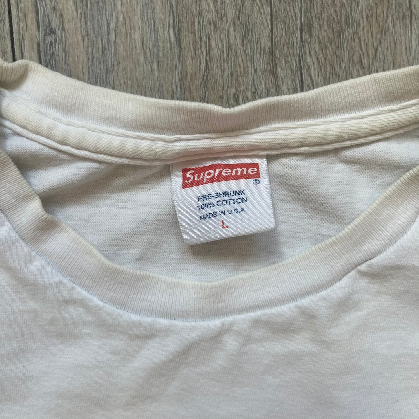 Supreme SS11 Mind Your Business White Tee is a white short-sleeve T-shirt from the Spring/Summer 2011 collection, made in the USA. The front features a graphic inspired by a whiskey label, including an old Supreme logo, a bust of an older man, a small “Mind Your Business” figure, and text referencing Supreme Bourbon Whiskeys with a New York address. This design is part of Supreme’s second delivery of SS11 T-shirts.