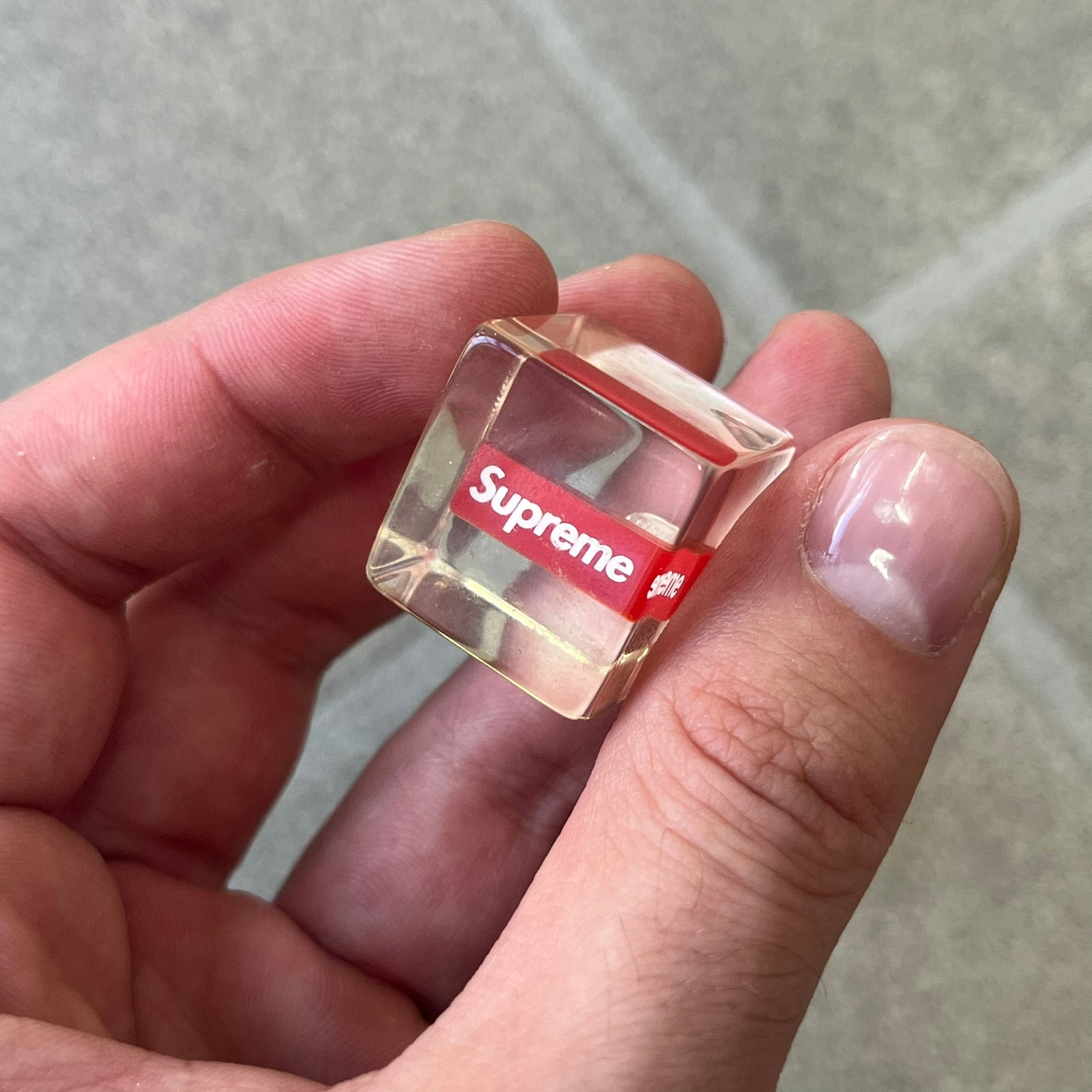 Supreme SS18 Hair Bobbles (Set of 2) features clear acrylic dice-shaped pieces with small red Supreme Box Logo details inside, attached to black elastic bands. The set includes two hair bobbles and comes in the original white Supreme box. Released on May 17, 2018.
