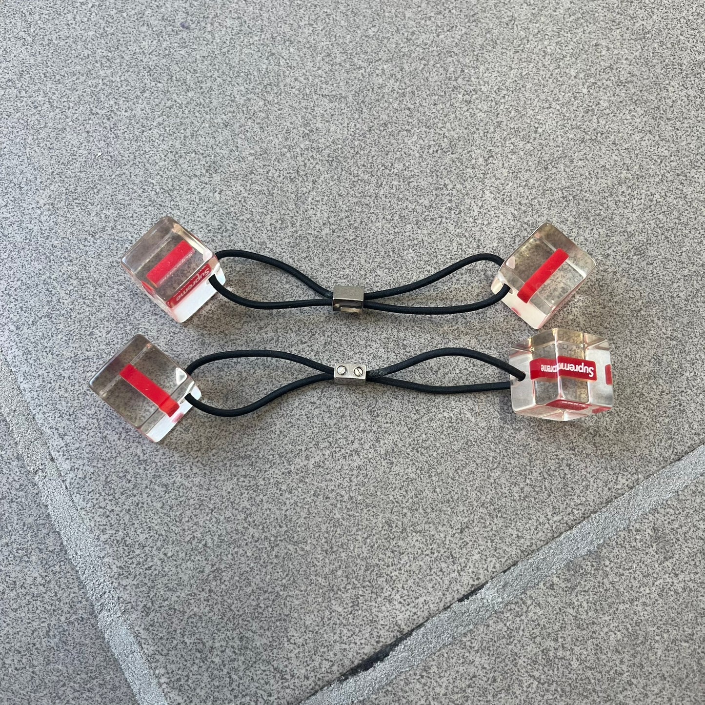 Supreme SS18 Hair Bobbles (Set of 2) features clear acrylic dice-shaped pieces with small red Supreme Box Logo details inside, attached to black elastic bands. The set includes two hair bobbles and comes in the original white Supreme box. Released on May 17, 2018.
