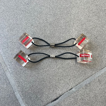 Supreme SS18 Hair Bobbles (Set of 2) features clear acrylic dice-shaped pieces with small red Supreme Box Logo details inside, attached to black elastic bands. The set includes two hair bobbles and comes in the original white Supreme box. Released on May 17, 2018.
