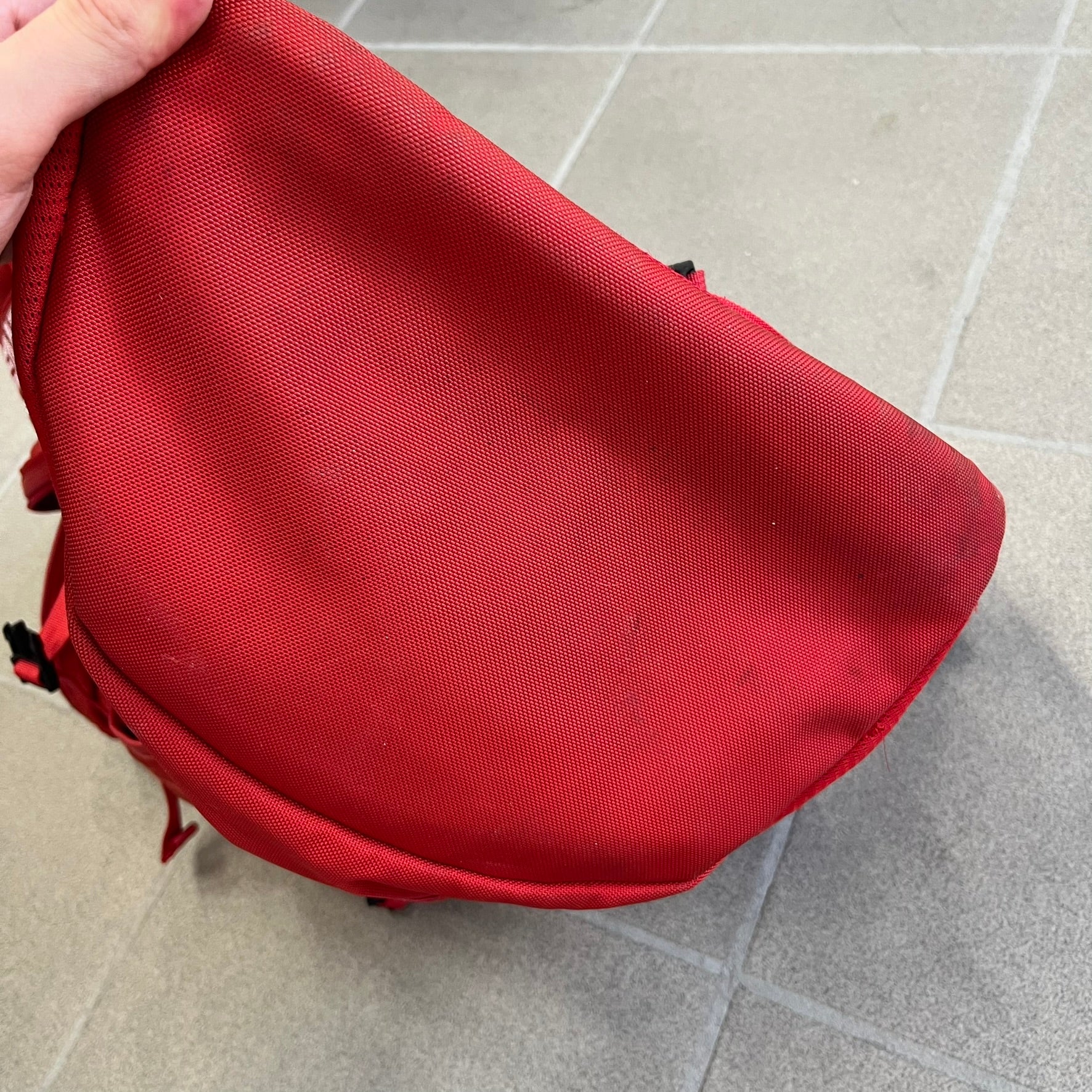 Supreme SS18 Red Backpack features a red construction with a large main compartment suitable for laptops and other larger devices, along with a front zippered pocket for smaller items. It has dual side mesh pockets and a Supreme Box Logo on the front.
