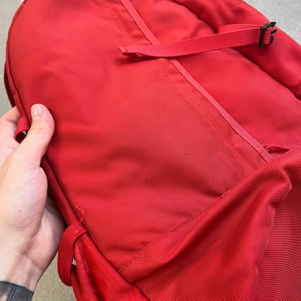 Supreme SS18 Red Backpack features a red construction with a large main compartment suitable for laptops and other larger devices, along with a front zippered pocket for smaller items. It has dual side mesh pockets and a Supreme Box Logo on the front.
