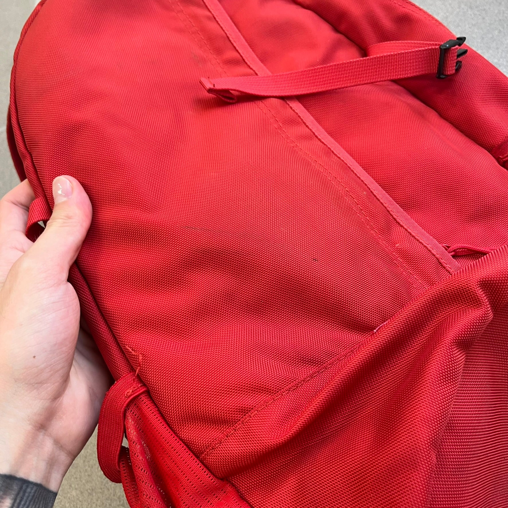 Supreme SS18 Red Backpack features a red construction with a large main compartment suitable for laptops and other larger devices, along with a front zippered pocket for smaller items. It has dual side mesh pockets and a Supreme Box Logo on the front.
